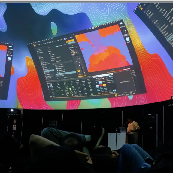 Menschen liegen in einem Kuppelraum, auf die Decke werden bunte Grafiken projiziert.