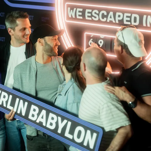 Gruppe jubelt vor Escape Room Schild, hält „Berlin Babylon“ Schild.