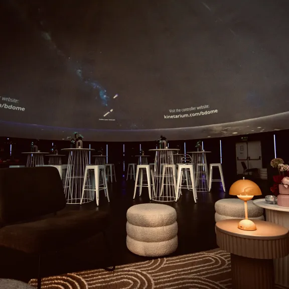 Gemütliche Lounge mit Sesseln, Hockern und Lampen unter einer Kuppel mit Sternenhimmel.