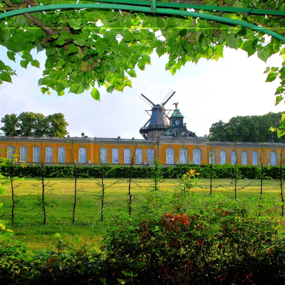 Green archway frames a windmill atop a yellow building, with grass and trees in front.