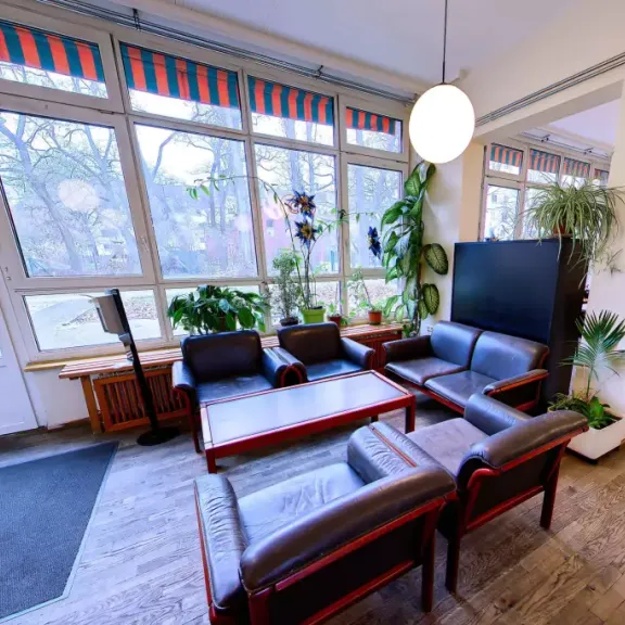 Heller Aufenthaltsraum mit modernen Sesseln, großem Fenster und Pflanzen.