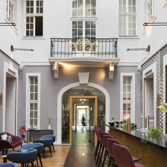 Heller, moderner Innenraum mit Bar, Barhockern und blauen Sesseln unter Glasdach.