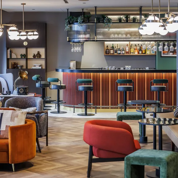 Moderne Hotelbar mit bunten Sesseln, Sofas und Barhockern, warme Beleuchtung