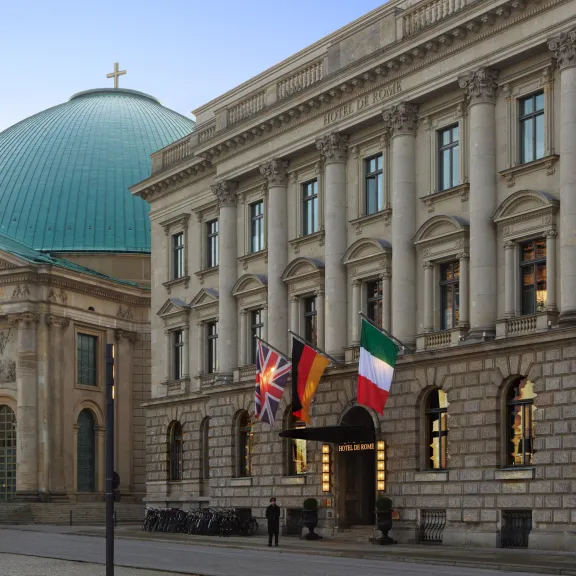 Historisches Gebäude mit vier Nationalflaggen, daneben eine Kuppelkirche im Hintergrund.