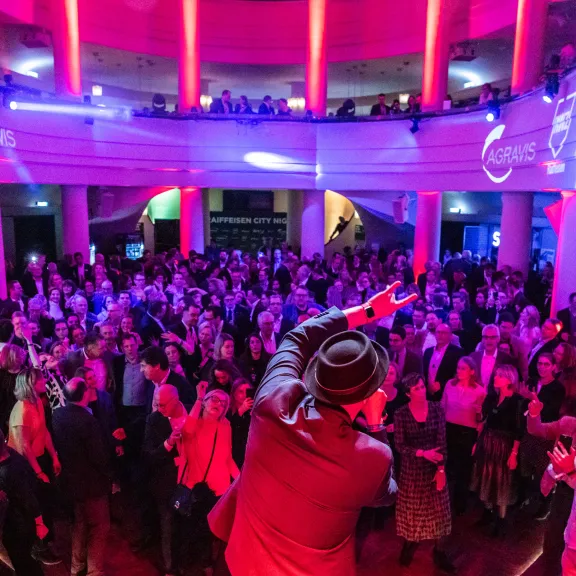 Menschenmenge auf einer Party mit bunter Beleuchtung und Musiker auf der Bühne.