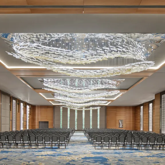 Großer, moderner Konferenzsaal mit Reihen schwarzer Stühle und dekorativen Deckenleuchten.