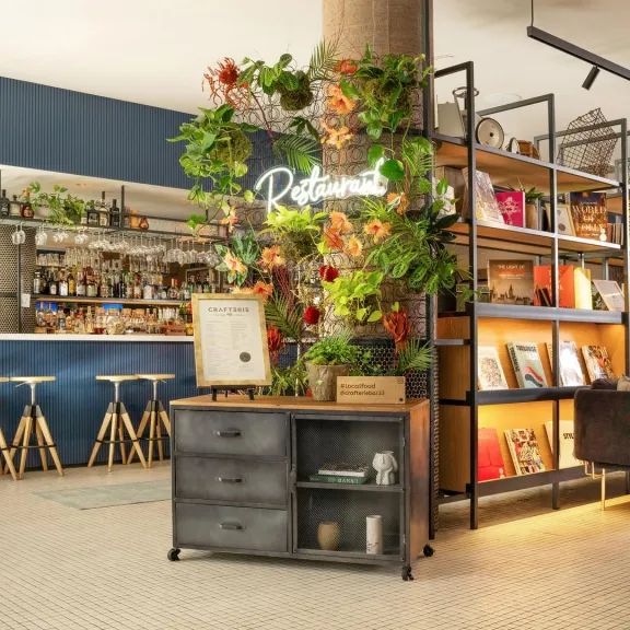 Modernes Café mit Pflanzen, Regal voller Bücher und gemütlicher Sitzecke.