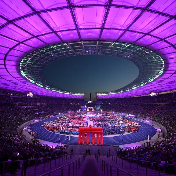 Das Berliner Olympiastadion mit violett beleuchtetem Dach, viele Menschen bei einer Großveranstaltung.