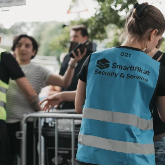 Sicherheitskräfte mit Warnwesten stehen vor einer Absperrung im Freien.