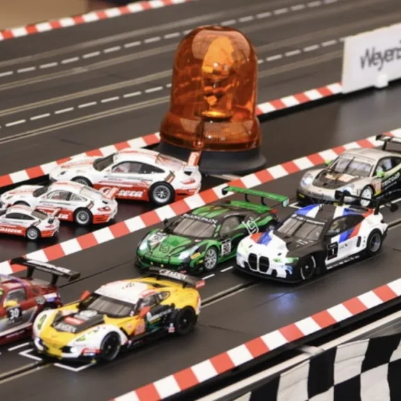Mehrere Modellrennwagen starten nebeneinander auf einer Carrera-Rennbahn.
