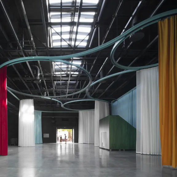 Großer Raum mit bunten Vorhängen und geschwungenen Rohren unter der Decke.