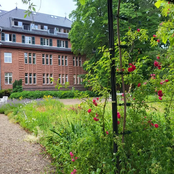 Rotes Backsteingebäude mit Garten, Blumen und Kletterrosen im Vordergrund.
