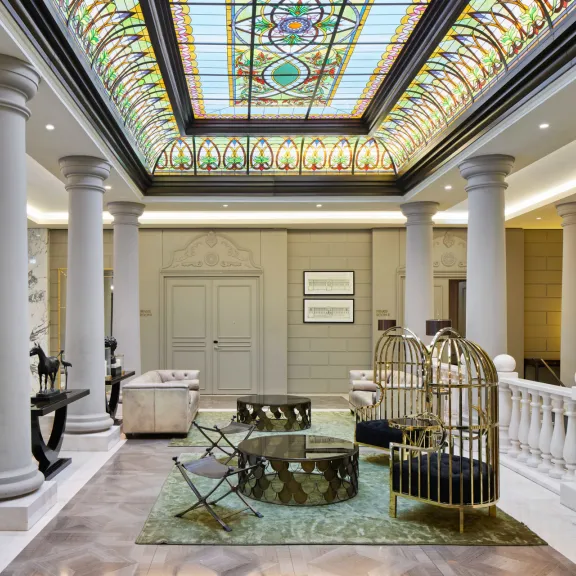 Elegante Hotellobby mit Marmorsäulen und buntem Glasdachfenster