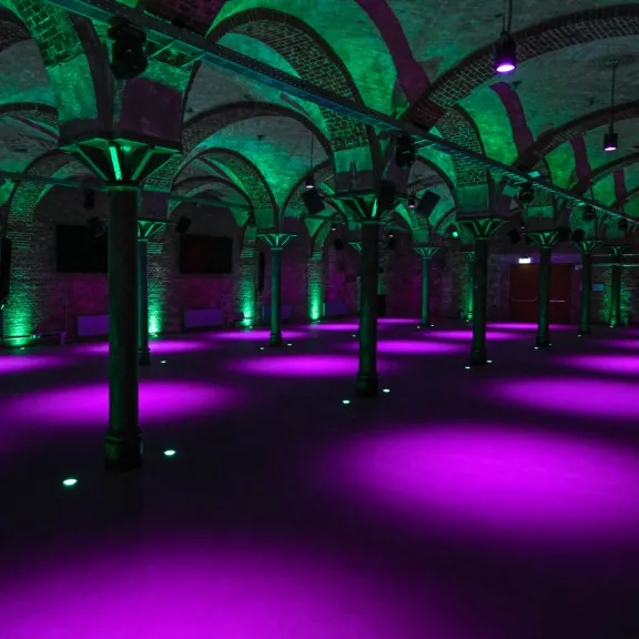 Gewölbekeller mit lila und grüner Beleuchtung, rotes VIP-Schild an der Wand.