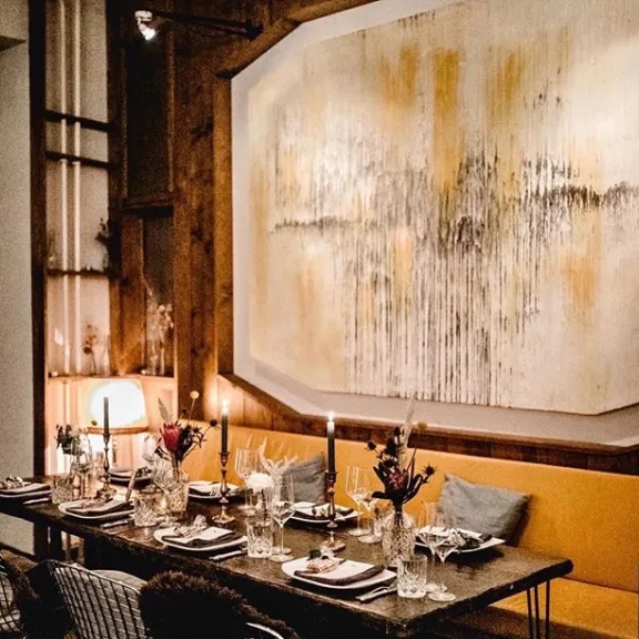 Elegant gedeckter Esstisch mit Kerzen, Bild mit abstrakter Kunst an der Wand.