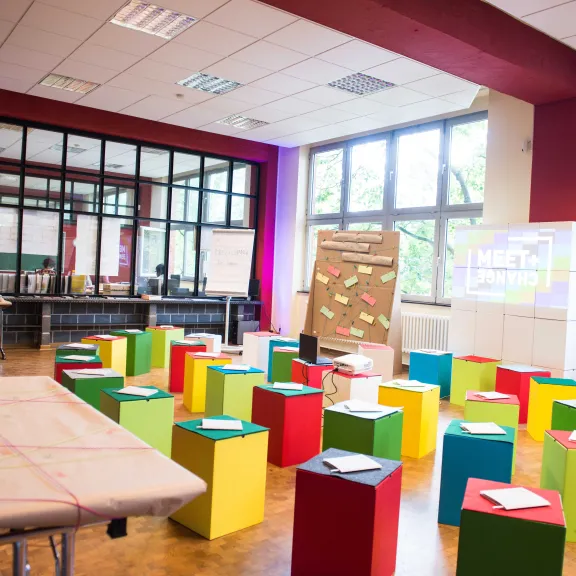 Heller Seminarraum mit bunten Würfeln als Sitzgelegenheiten und großen Fenstern.