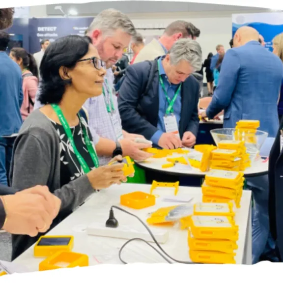 Menschen bei einer Messe, stehen an Tischen mit gelben Schachteln und Unterhaltungen.