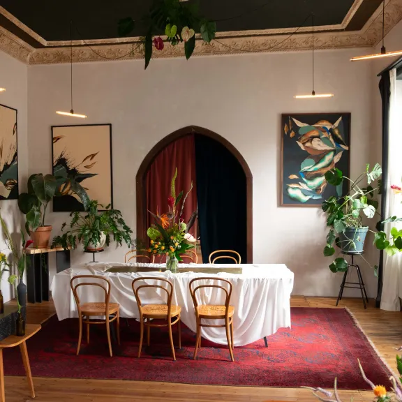 Stilvoll gedeckter Tisch in einem hellen Raum mit Pflanzen und Kunstwerken an den Wänden.