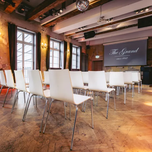 Heller Konferenzraum mit weißen Stühlen, Leinwand und großen Fenstern