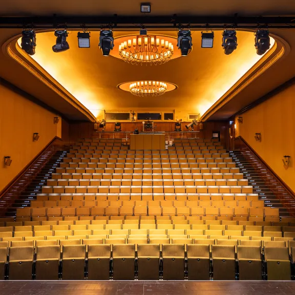 Leerer Kinosaal mit gelben Sitzen und zwei Kronleuchtern an der Decke.
