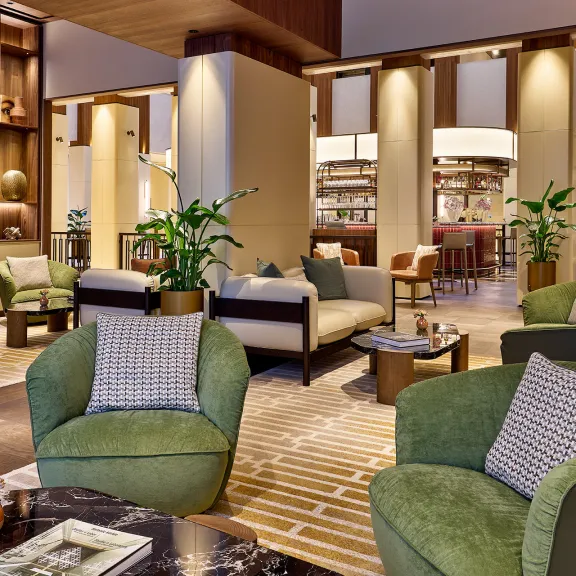 Modern eingerichtete Hotellobby mit grünen Sesseln, Pflanzen und warmem Licht.