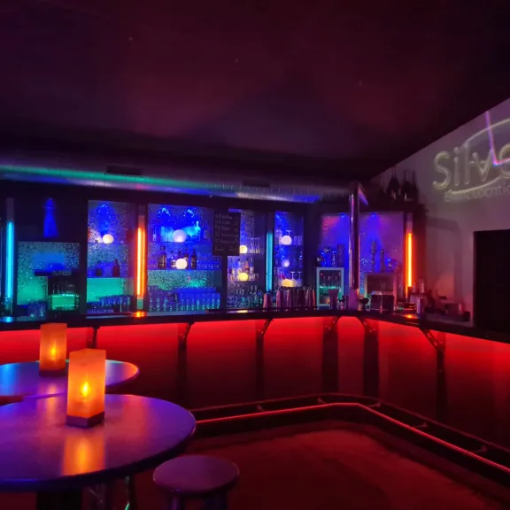 Stimmungsvolle Bar mit buntem Licht, leeren Tischen und Kerzen.