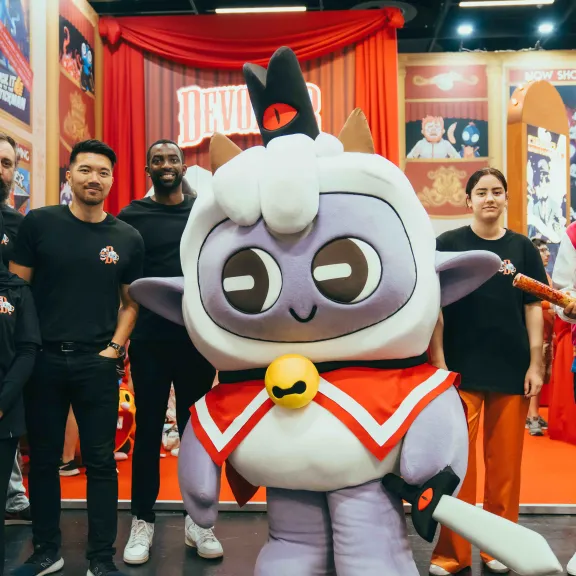 Gruppe von Menschen posiert neben einem großen, bunten Maskottchenkostüm.