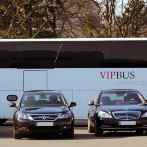 Mehrere schwarze Limousinen und ein großer VIP-Reisebus auf einem Parkplatz.