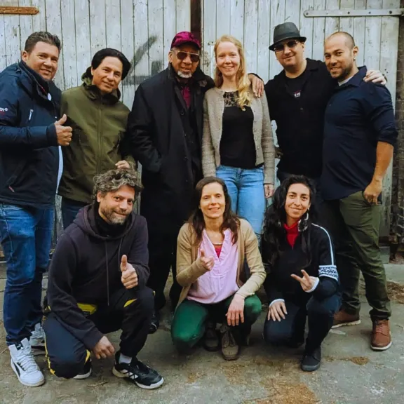 Neun lächelnde Menschen posieren vor einer alten Holztür auf einem Hinterhof.
