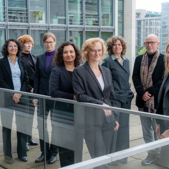 Neun Personen in Businesskleidung stehen draußen vor modernen Bürogebäuden.