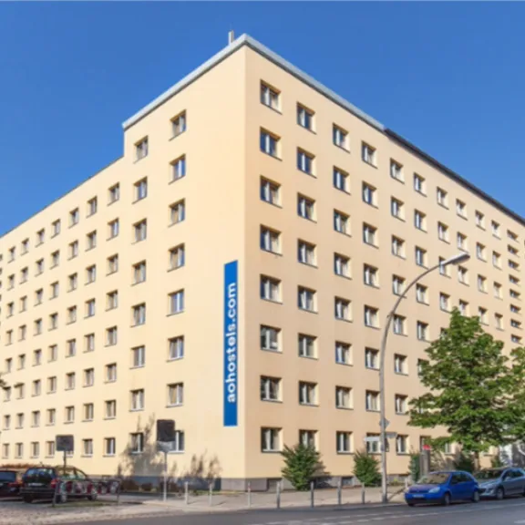 Großes, beiges Hotelgebäude mit mehreren Stockwerken an einer Straßenecke bei Sonnenschein.