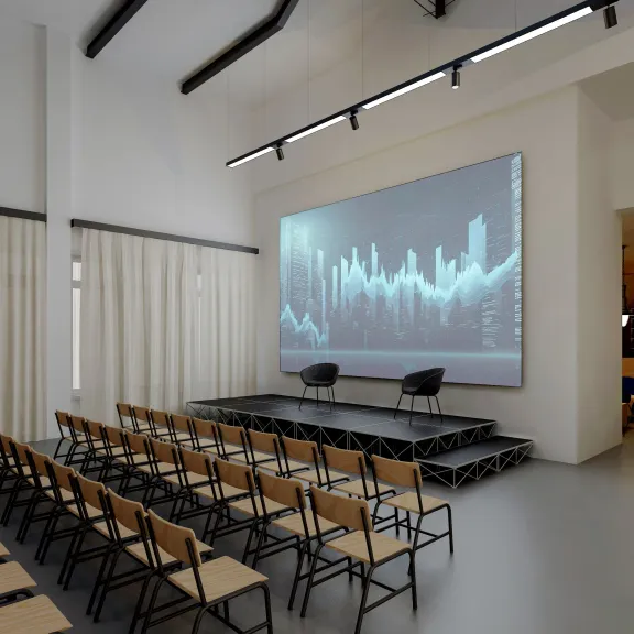 Moderner Konferenzraum mit Reihen aus Stühlen, Bühne und großem Bildschirm