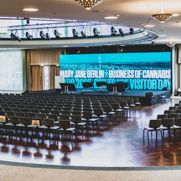 Moderner Veranstaltungssaal mit leeren Stuhlreihen und großer LED-Bühne.