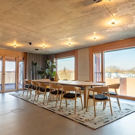Moderner Konferenzraum mit langem Holztisch, Stühlen und großen Fenstern mit Ausblick.