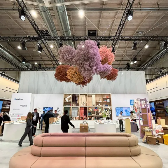 Moderne Messehalle mit beiger Couch und schwebender Blumendekoration in Rosa und Orange.