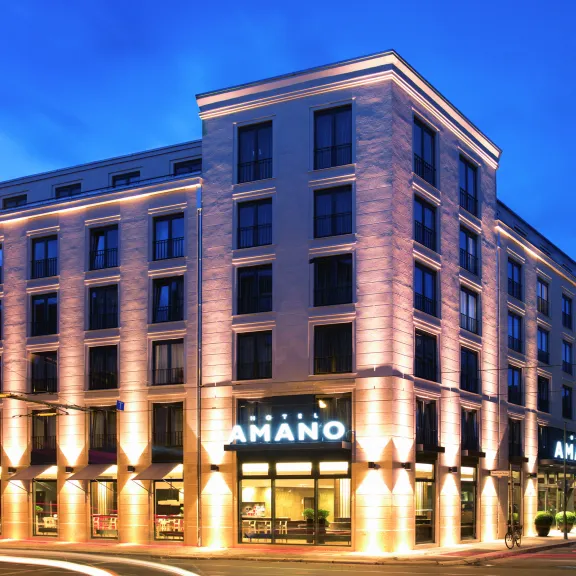 Modern hotel building illuminated at night with "Amano" sign above the entrance.