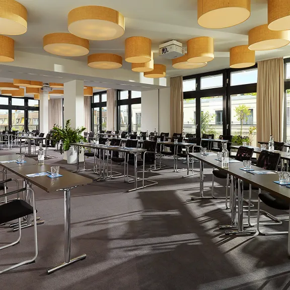 Heller Konferenzraum mit vielen Tischen, Stühlen und großen Fenstern