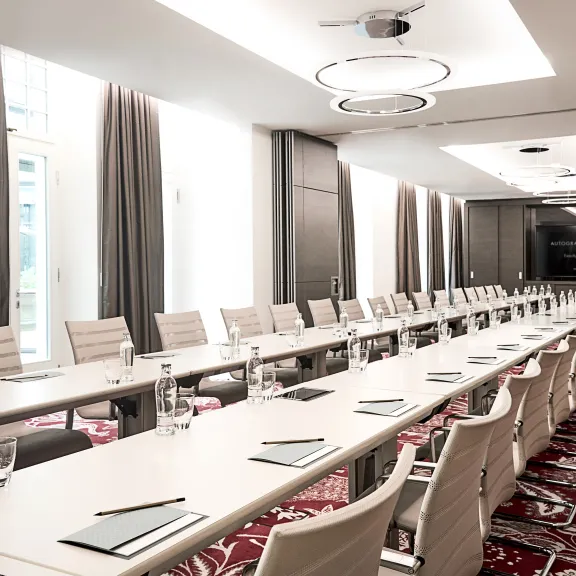 Konferenzraum mit langen Tischen, weißen Stühlen und moderner Beleuchtung