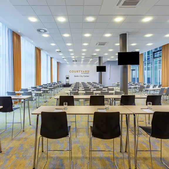 Moderner, heller Konferenzraum mit vielen leeren Tischen und Stühlen.