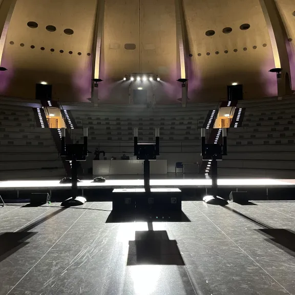 Leerer Vortragssaal mit Podium und lila Beleuchtung, Blick von der Bühne.