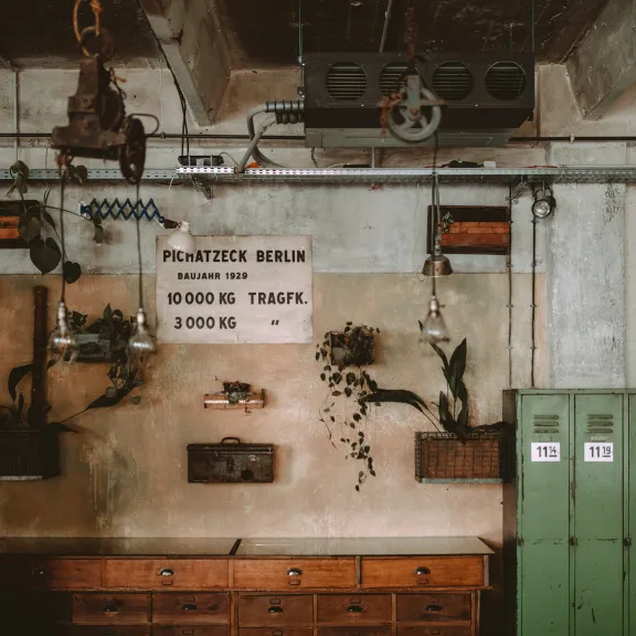 Werkloft Alte Werkstatt mit grünen Spinden, Holztisch und Wanddeko unter industrieller Decke.