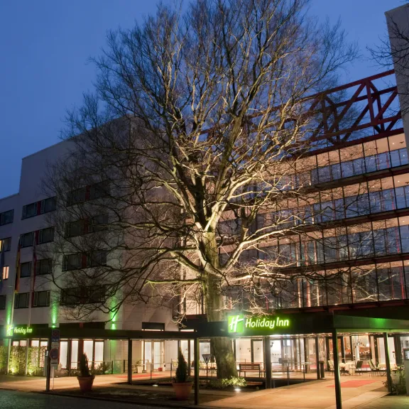 Modern hotel exterior with large lit tree and glass entrance at dusk.