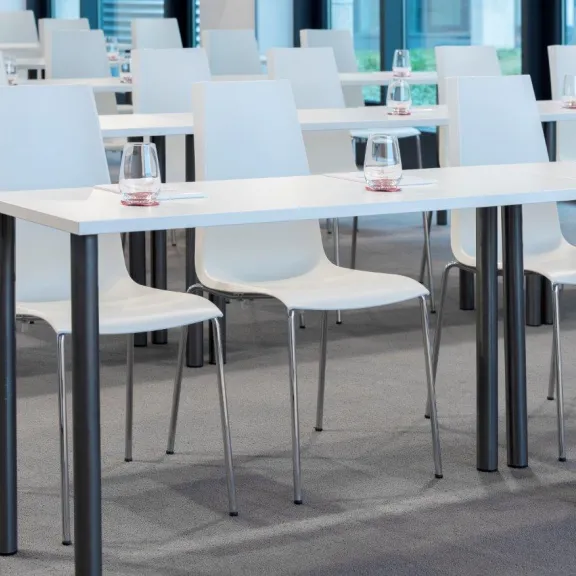Helle Seminarraumreihe mit weißen Stühlen und Tischen, Wassergläser bereitgestellt.