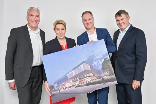 Four people present an architectural rendering of a modern convention center