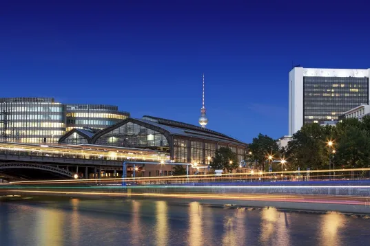 Cityscape with modern buildings, a bridge, and a river at dusk under a clear sky.