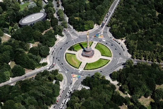 Aerial view of a circular monument surrounded by roads and dense green trees.