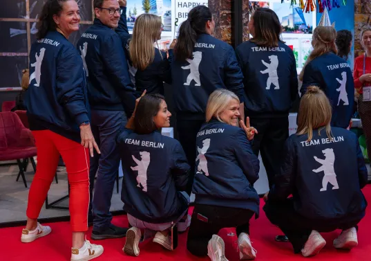 Team des visitBerlin Berlin Convention Office mit Berlin-Jacken auf rotem Teppich bei einer Messe