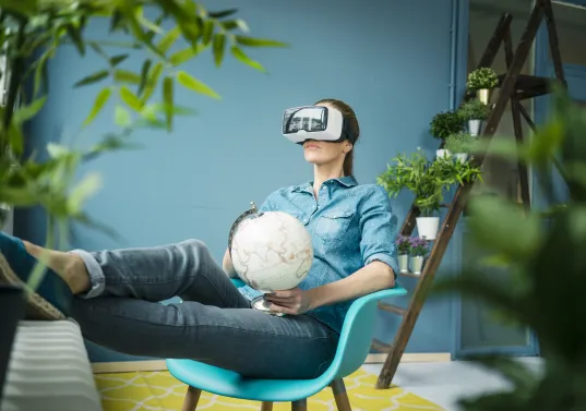 Frau mit VR-Brille hält Globus und sitzt entspannt auf einem Stuhl im modernen Raum.