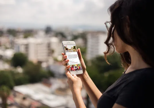 Woman holding a smartphone, overlooking a cityscape on a sunny day.