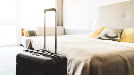 Suitcase by a neatly made bed in a bright hotel room.
